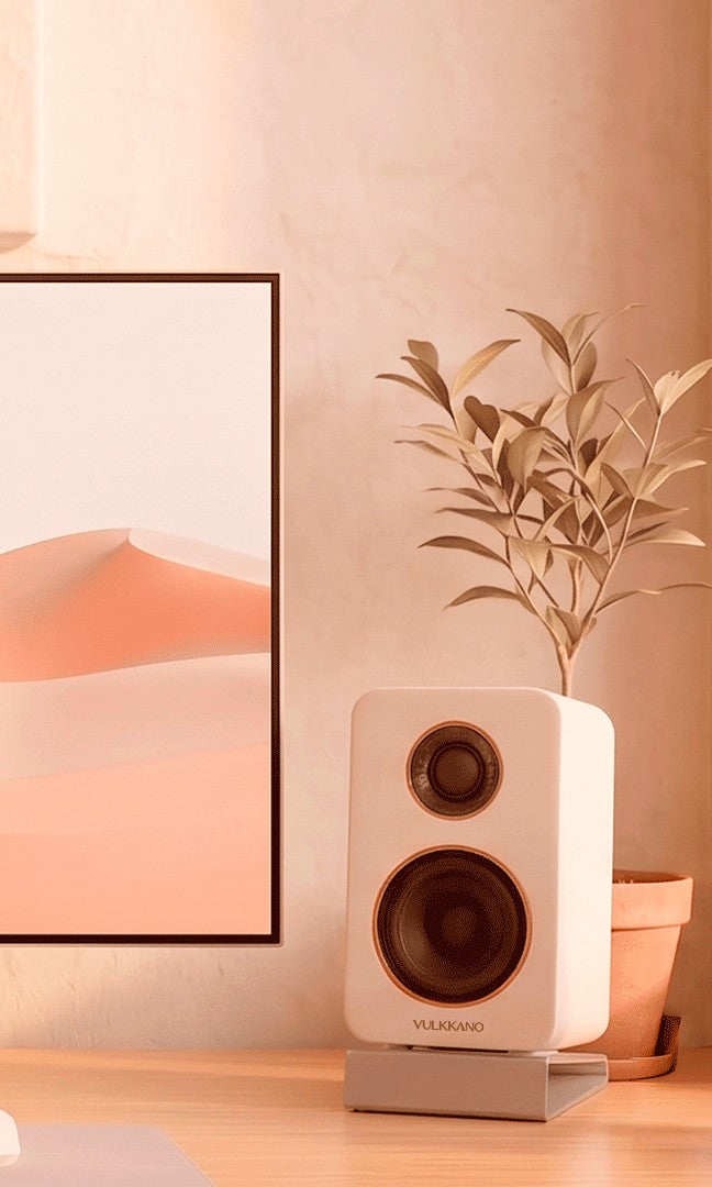 Altavoces VULKKANO DESK blancos en un escritorio junto a un monitor